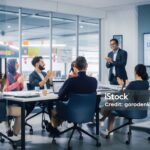 Multi-Ethnic Office Conference Room. Indian CEO does Presentation for Diverse Young Entrepreneurs, Talking, Using TV with Infographics, Statistics, Graphs. Businesspeople Invest in e-Commerce Startup